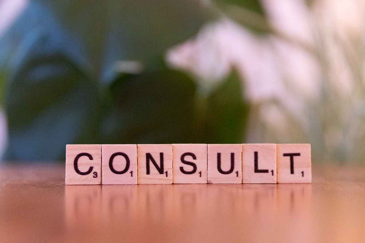 Home Scrabble tiles spelling 'CONSULT' on a wooden table with blurred background.