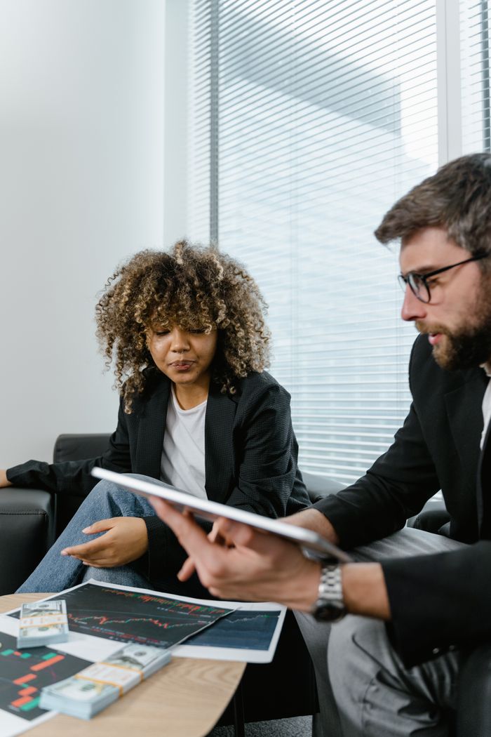Contact Two professionals discussing financial graphs on a tablet in a modern office setting.